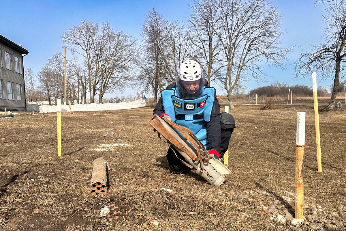 FSD deminer wearing a blue protective vest and visors conducts a survey in the UA Swiss Kharkiv Pryshyb Territory.